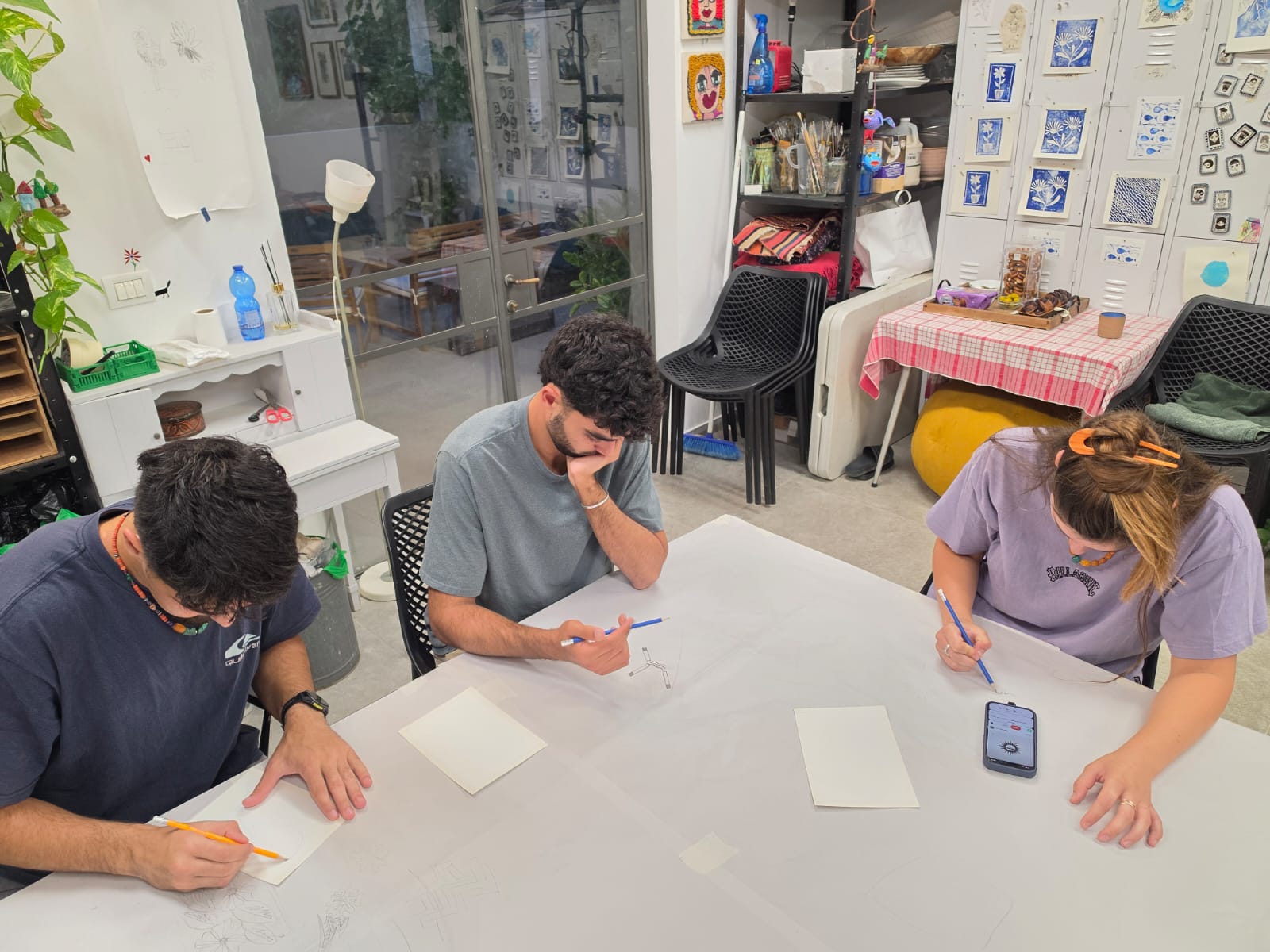 שלושה משתתפים יוצרים בריכוז סביב שולחן רישום